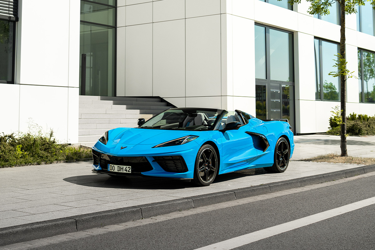 Blaue Chevrolet Corvette C8 Cabrio steht an einer modernen Gebäude-Fassade.