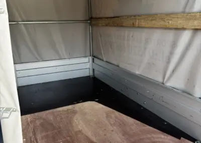 Inneres eines leeren Anhängers mit Holzrahmen und grauem Bodenbelag.