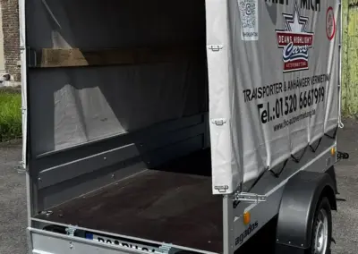 Offener Anhänger mit abnehmbarer Plane, ausgestattet mit einer stabilen Ladefläche und einem Rad.
