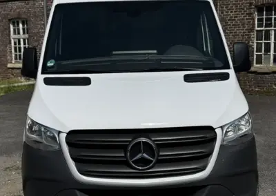 Frontansicht eines weißen Mercedes Sprinter Transporters mit einem Nummernschild.