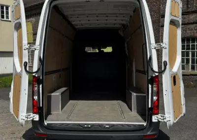 Innenansicht eines leeren Transporters mit offenen Hecktüren und Holzverkleidung.