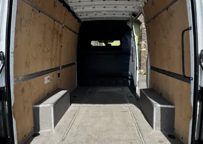 Innenansicht eines leeren Transporters mit Holzverkleidung und zwei Sitzbänken.