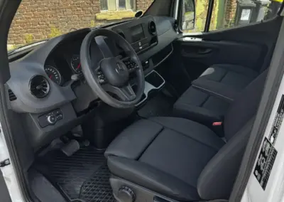 Innenraum eines Mercedes Sprinter mit zwei Sitzen und Armaturenbrett sichtbar.