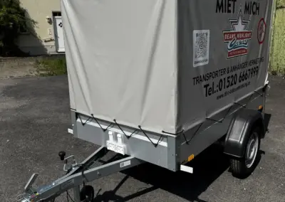 Ein Anhänger mit einer grauen Plane und einem Aufdruck für Transportdienste auf einem Parkplatz.