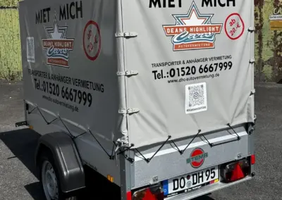 Grauer Stema Anhänger mit Plane und Werbeaufdruck für Autovermietung.