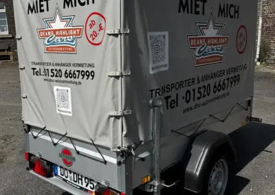 Ein Stema Anhänger mit grauer Plane und Werbeaufdruck für Mietservice in Deutschland.
