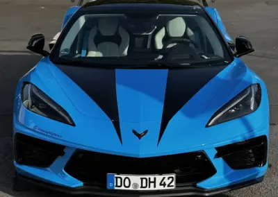 Blaue Chevrolet Corvette C8 mit schwarzem Streifen und weißen Sitzen, frontal aufgenommen.