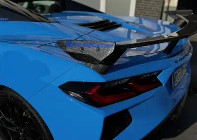 Blauer Chevrolet Corvette C8 mit Kohlefaser-Heckspoiler und sportlichem Design.