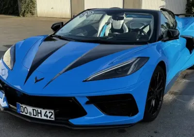 Blauer Chevrolet Corvette C8 mit schwarzem Dach und sportlichem Design auf einem Parkplatz.