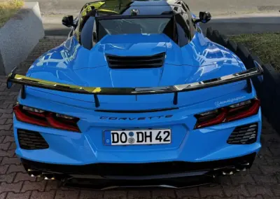 Ein blauer Corvette Sportwagen von hinten mit einem schwarzen Spoiler und einem Kennzeichen aus Dortmund.