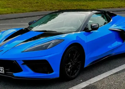Blauer Chevrolet Corvette C8 mit schwarzem Dach und sportlichem Design auf der Straße.