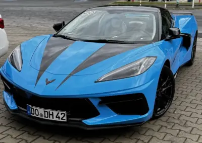Blauer Chevrolet Corvette C8 mit schwarzem Dach und Streifen auf einem Parkplatz.
