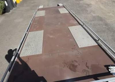 Offener Autotransportanhänger mit Auffahrrampen und rutschfesten Metallflächen auf einem Hof neben Mietfahrzeugen