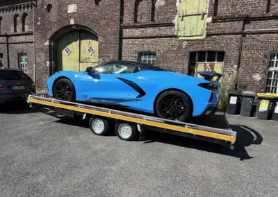Blauer Sportwagen steht auf einem zweiachsigen Autotransportanhänger vor einer historischen Backsteinhalle in Dortmund.