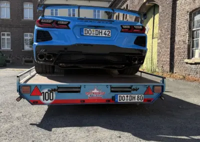 Blauer Chevrolet Camaro mit Kennzeichen DO-DH 42 steht auf einem rot-blauen Autotransportanhänger im Innenhof.